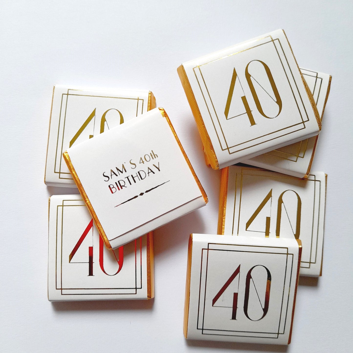 May include: Gold foil chocolate bar wrappers with a white background and gold lettering. The wrappers feature the number "40" and the text "Sam's 40th Birthday".