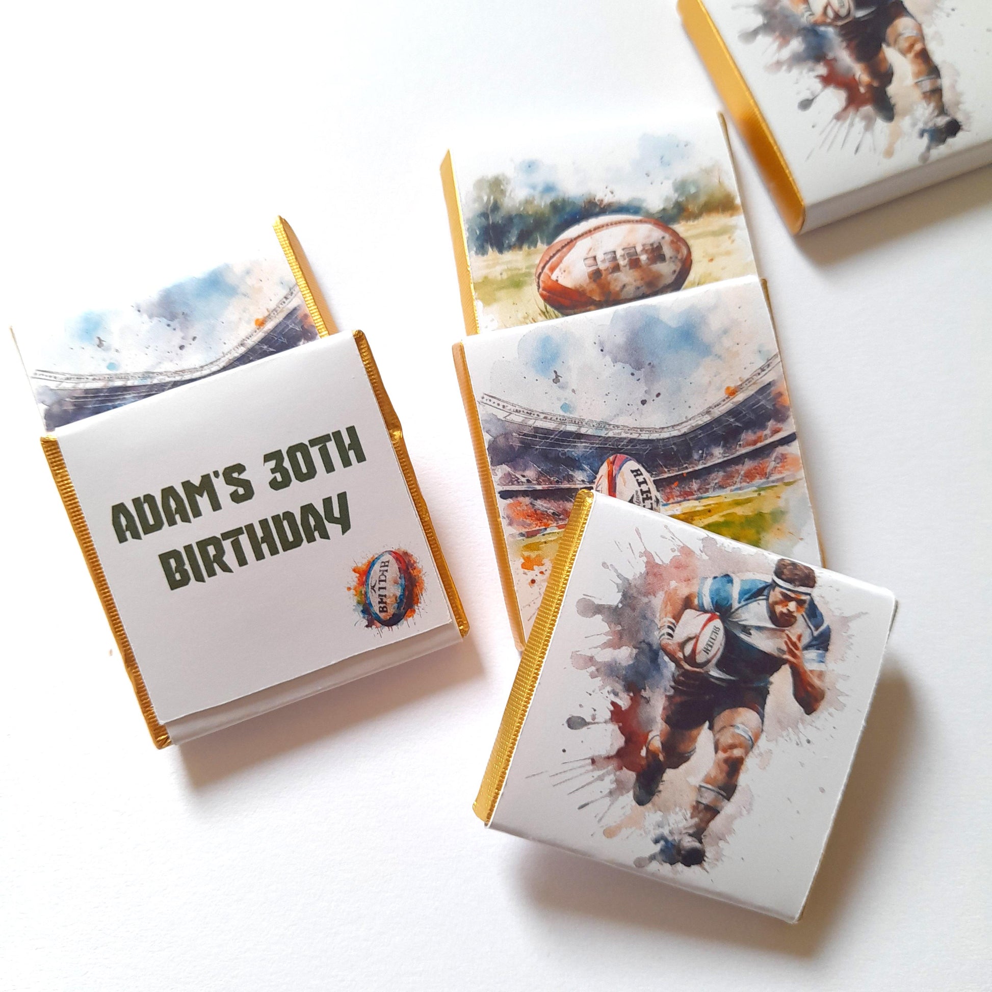 May include: A set of six personalised chocolate bars with a rugby theme. The bars feature watercolour illustrations of rugby players and balls. One bar has the text "Adam's 30th Birthday".