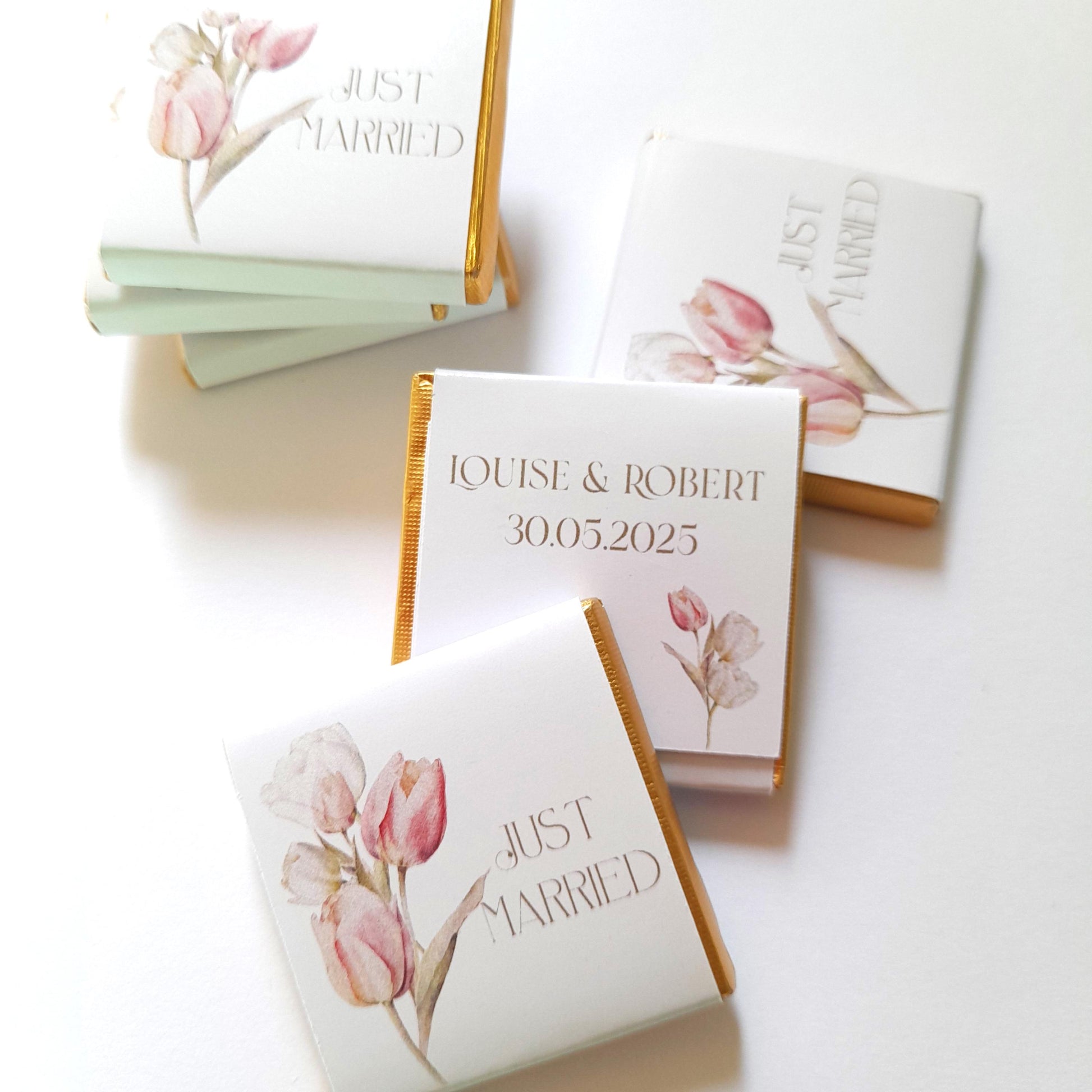 May include: White chocolate bar wrappers with a watercolour floral design featuring pink tulips. The wrappers have gold foil accents and the text "Just Married" and "Louise & Robert 30.05.2025".