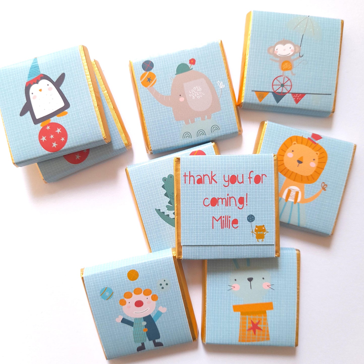 May include: Light blue chocolate wrappers with gold edges, decorated with circus animal illustrations. Designs include a penguin, elephant, monkey, lion, crocodile, and a clown. One wrapper reads "thank you for coming! Millie".