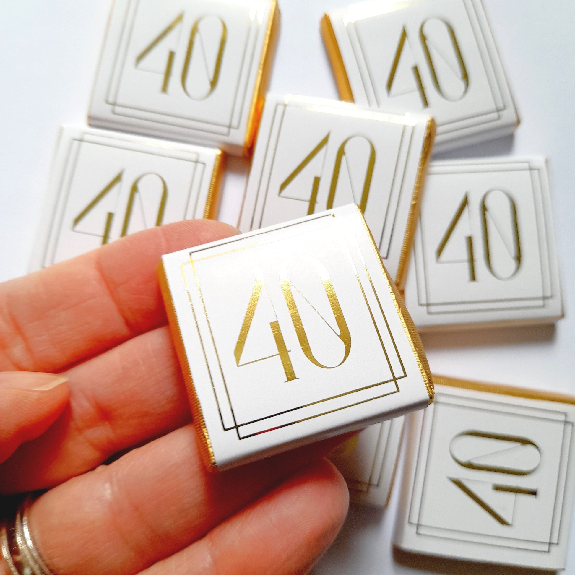 May include: A close-up of a white chocolate bar with a gold border and the number "40" printed in gold. The chocolate bar is surrounded by other similar chocolate bars.