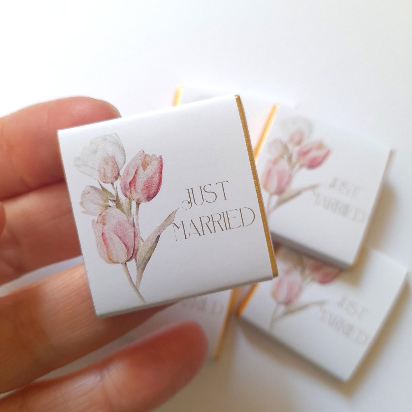 May include: White favour boxes with gold trim and pink watercolour tulips. The boxes have the text "Just Married" printed on them.